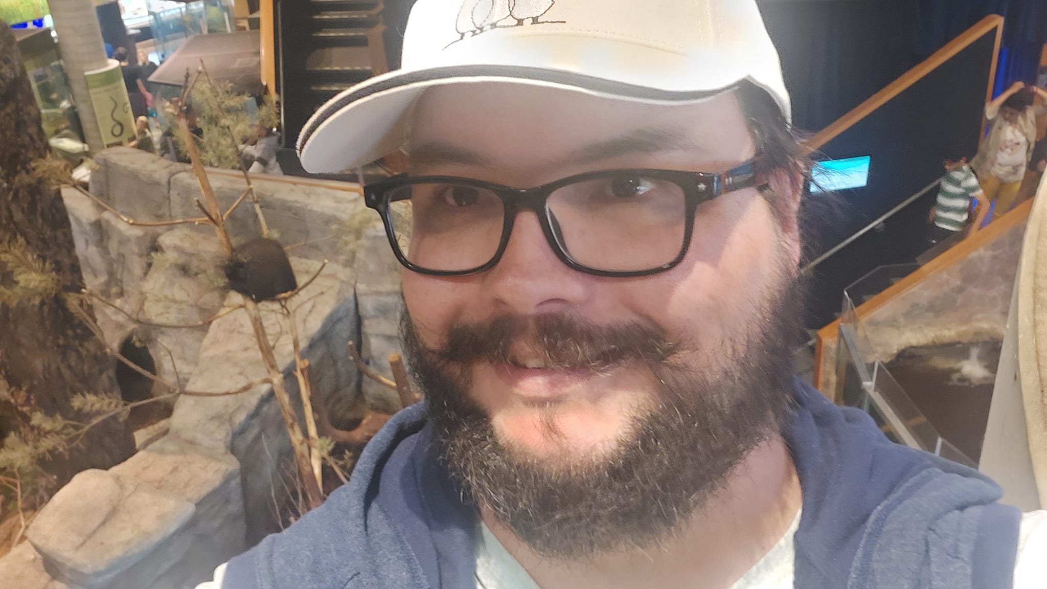 A man with a ball cap and bushy facial hair is standing in front of the porcupine, but from a higher floor than the last photo